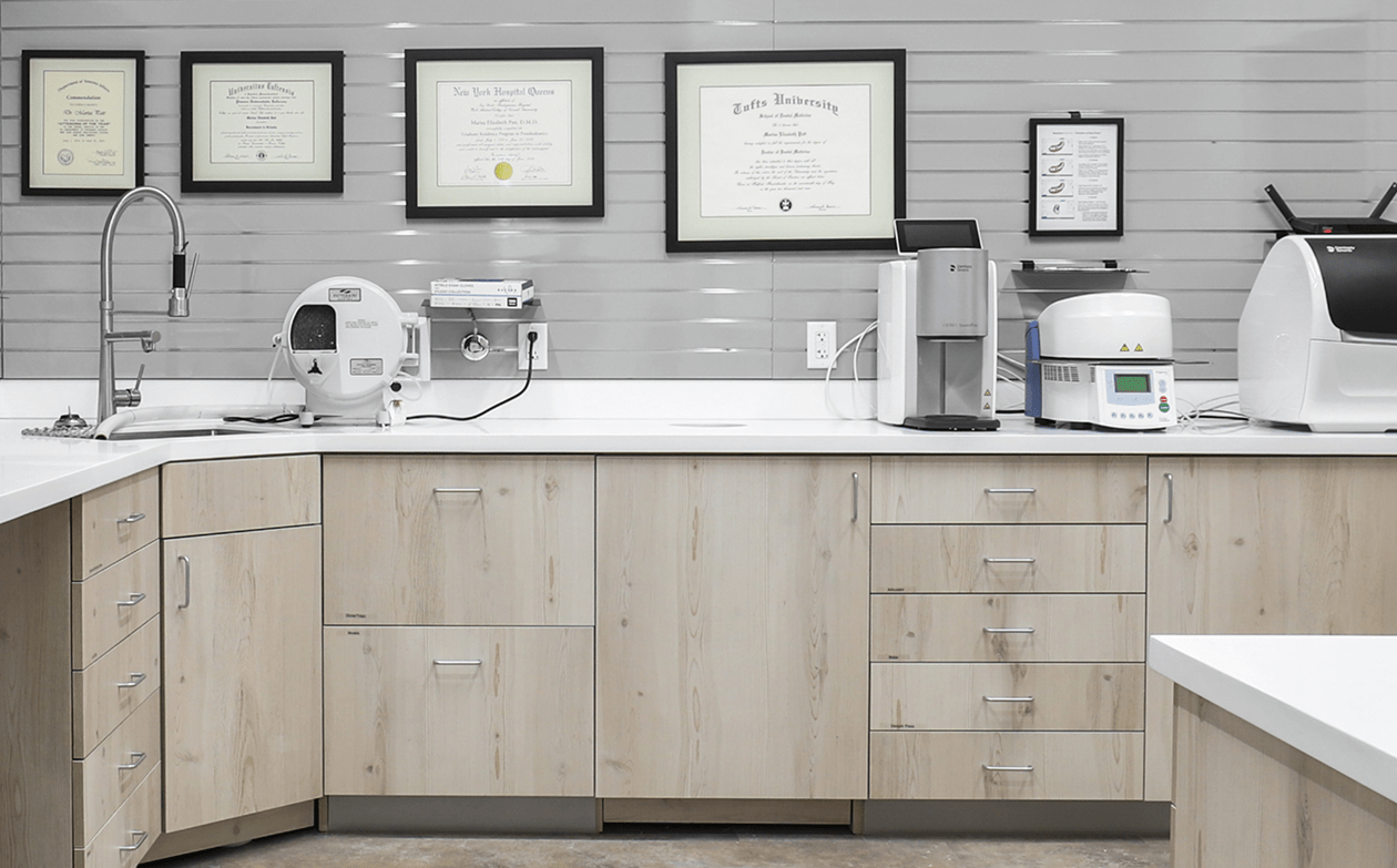 Clean dental office lab with light wood cabinets, dental equipment on counters, and framed certificates on gray walls, conveying professionalism.