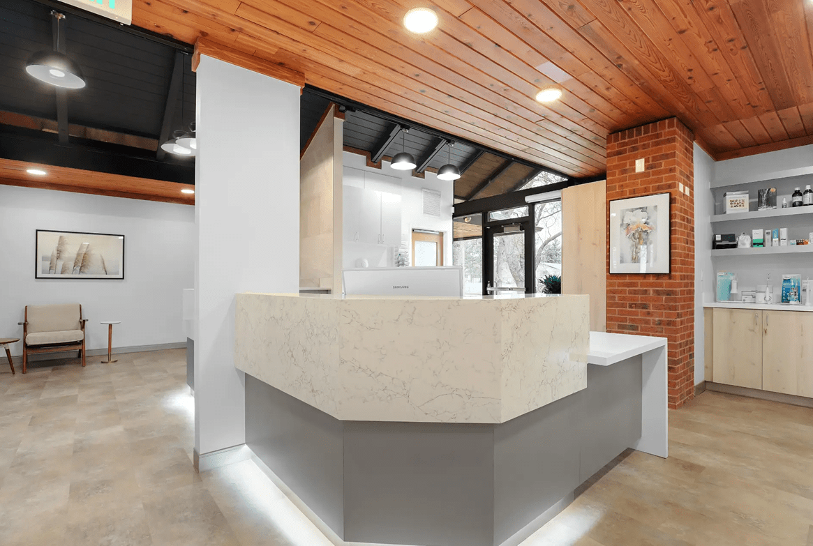 Modern office reception area with a marble desk, wood-paneled ceiling, and brick accent wall. Warm tones and natural light create a welcoming atmosphere.