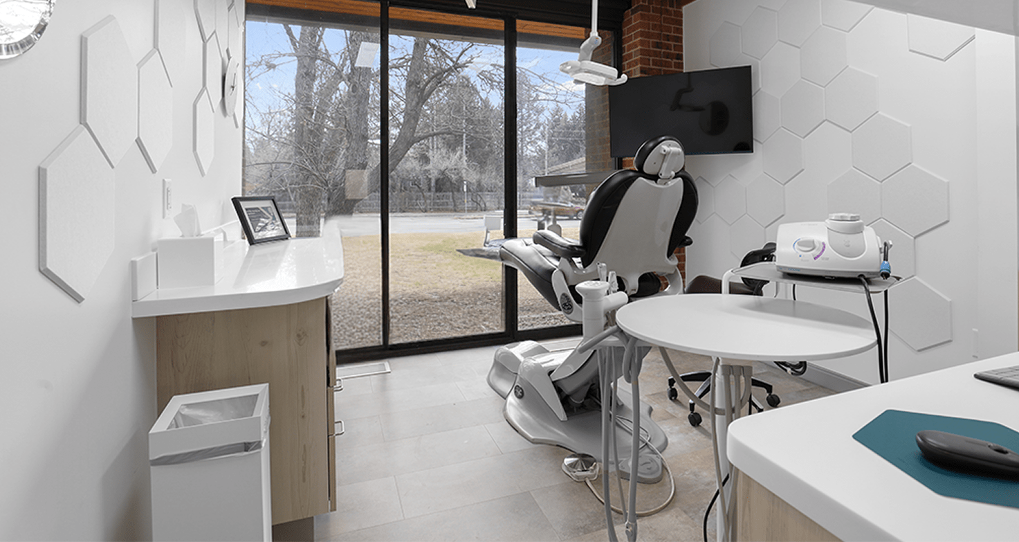 Modern dental office with a sleek chair, large window offering a view of trees, white hexagonal wall patterns, and a calm, professional ambiance.