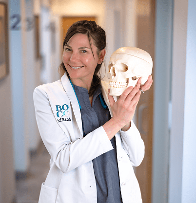 Dr. Patt in a white coat holds a human skull model, demonstrating an engagement in dental education within a clinical setting.