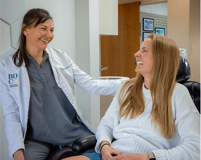 Dr. Patt in a white lab coat gently interacts with a seated patient in a modern dental office.